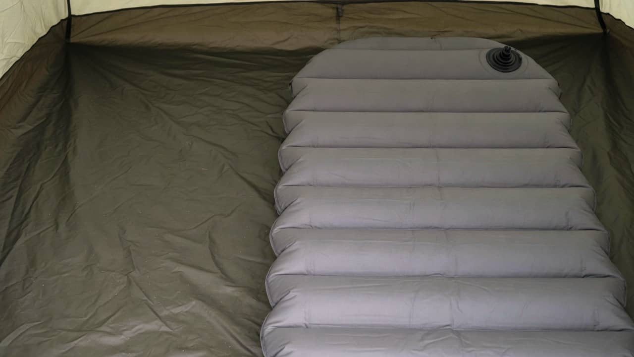 An inflated grey air pad with a round valve in the right half of a tent floor, darker empty floor on the left