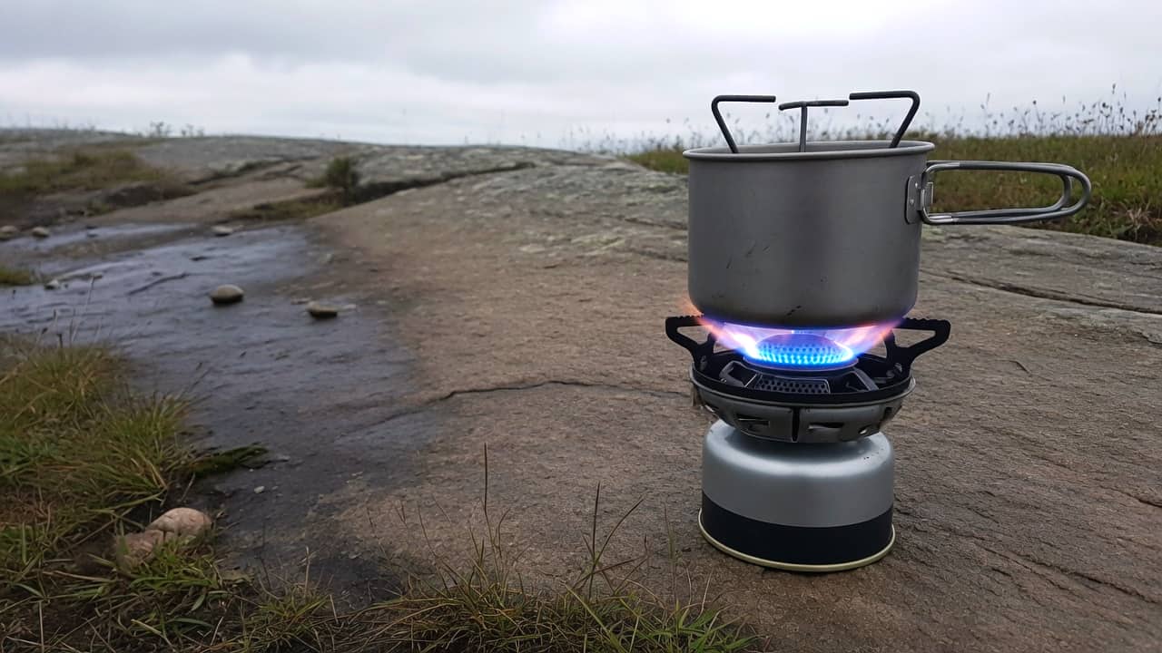 A canister stove with a blue flame and a metal pot on a rock in the right half, darker stone on the left